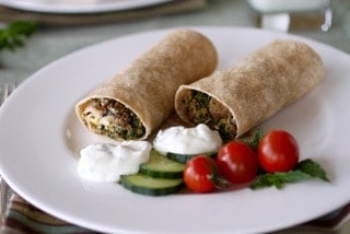 Gyros Breakfast Burritos on a plate with yogurt dressing and cucumber and tomatoes