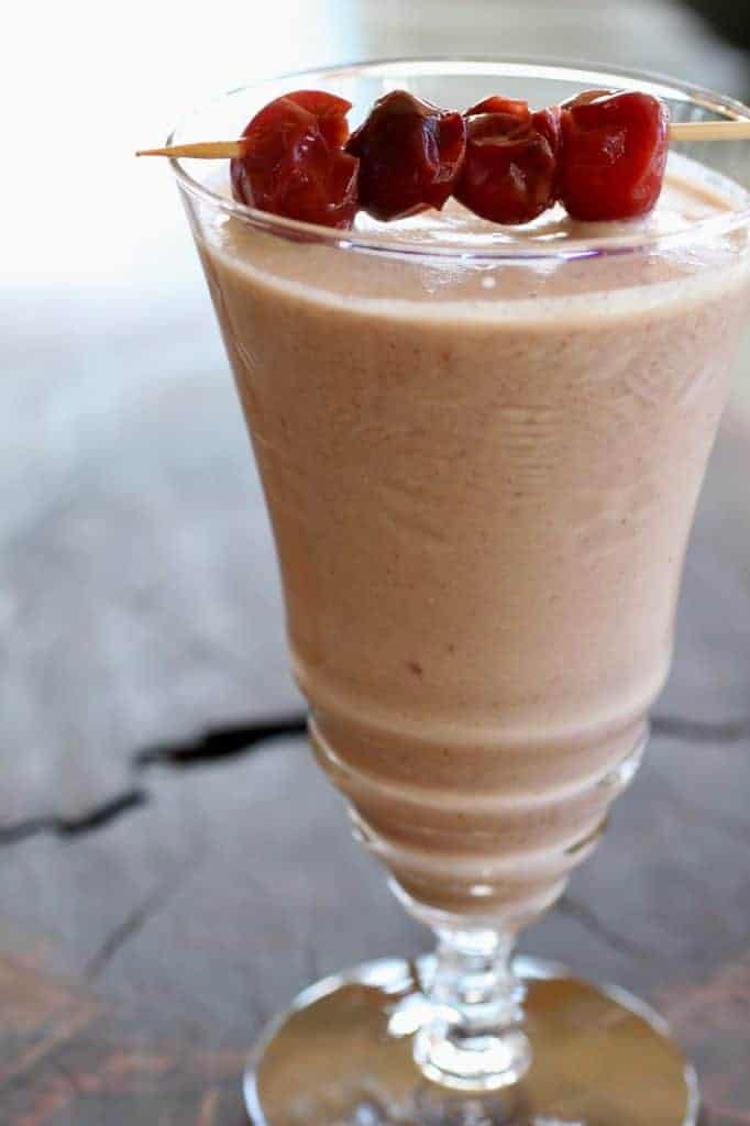Cherry Amaranth Almond Smoothie in a glass with cherries threaded on a. toothpick