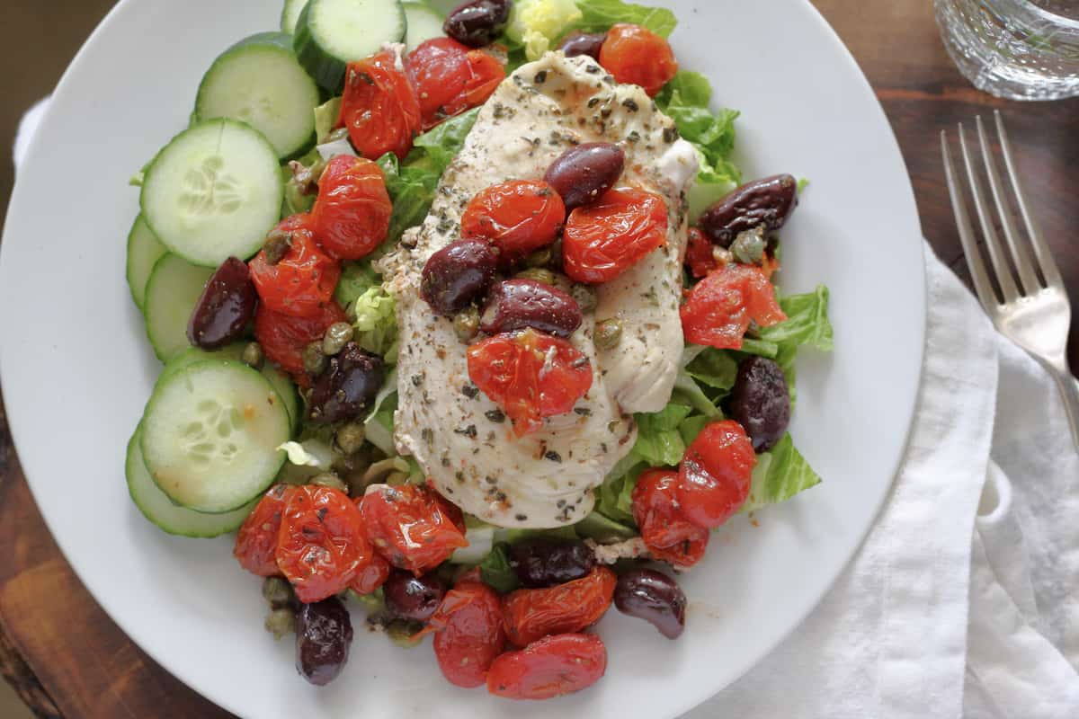 plate of herbed chicken with cooked tomatoes and kalamate olive over lettuce and cucumbers