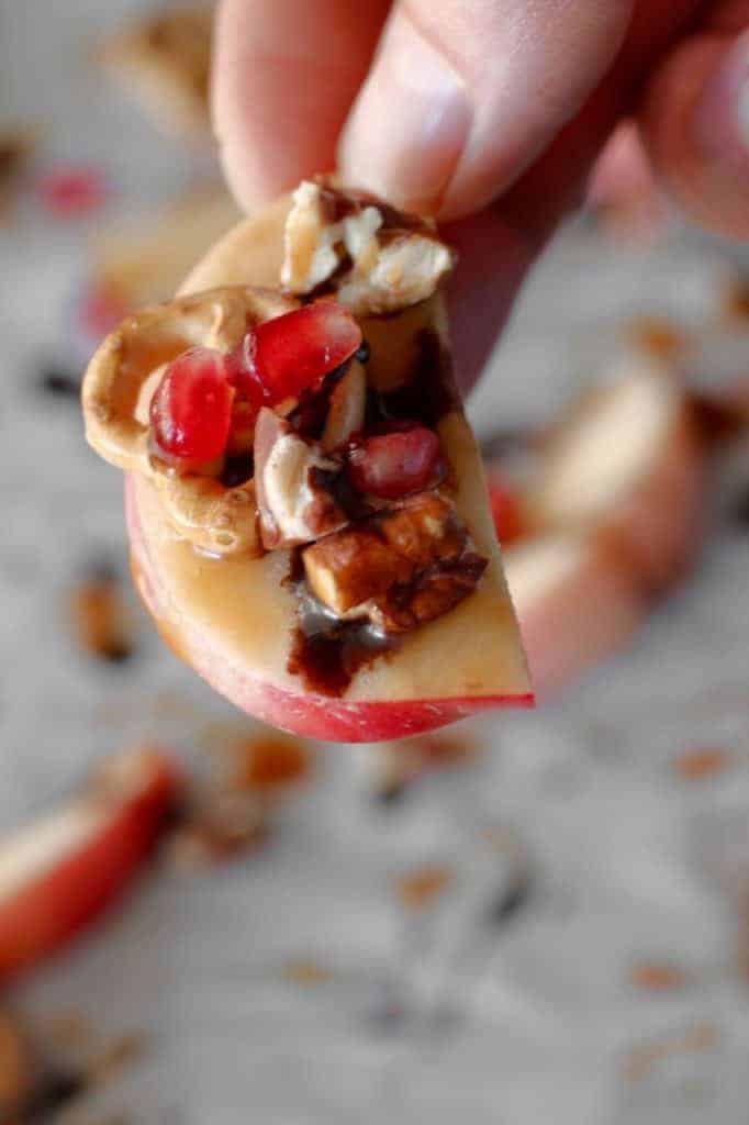 an apple slice with pecans, pretzel, pomegranate and chocolate syrup 