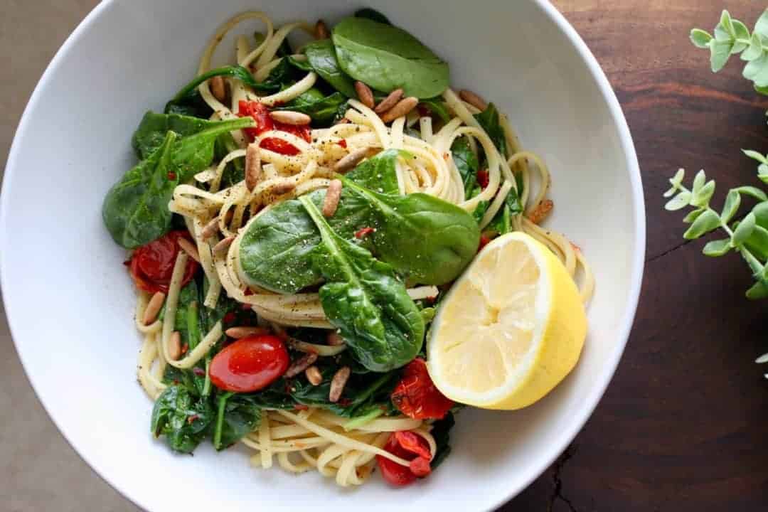 a bowl of spaghetti with spinach, blistered tomatoes and pine nuts