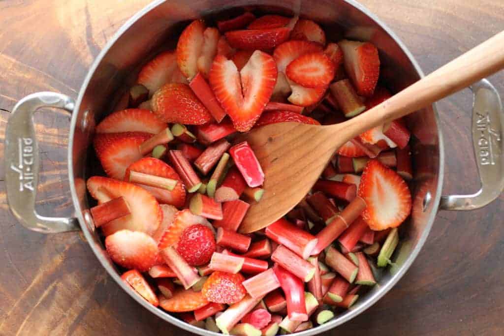 fresh chopped strawberries and rhubarb in a pan with wooden spoon