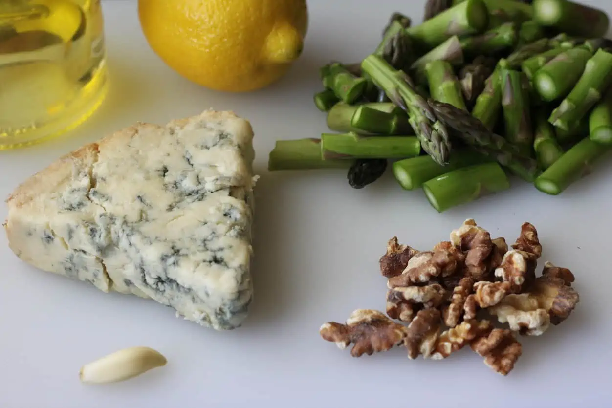 blue cheese wedge, lemon, asparagus, walnuts, garlic an olive oil on cutting board