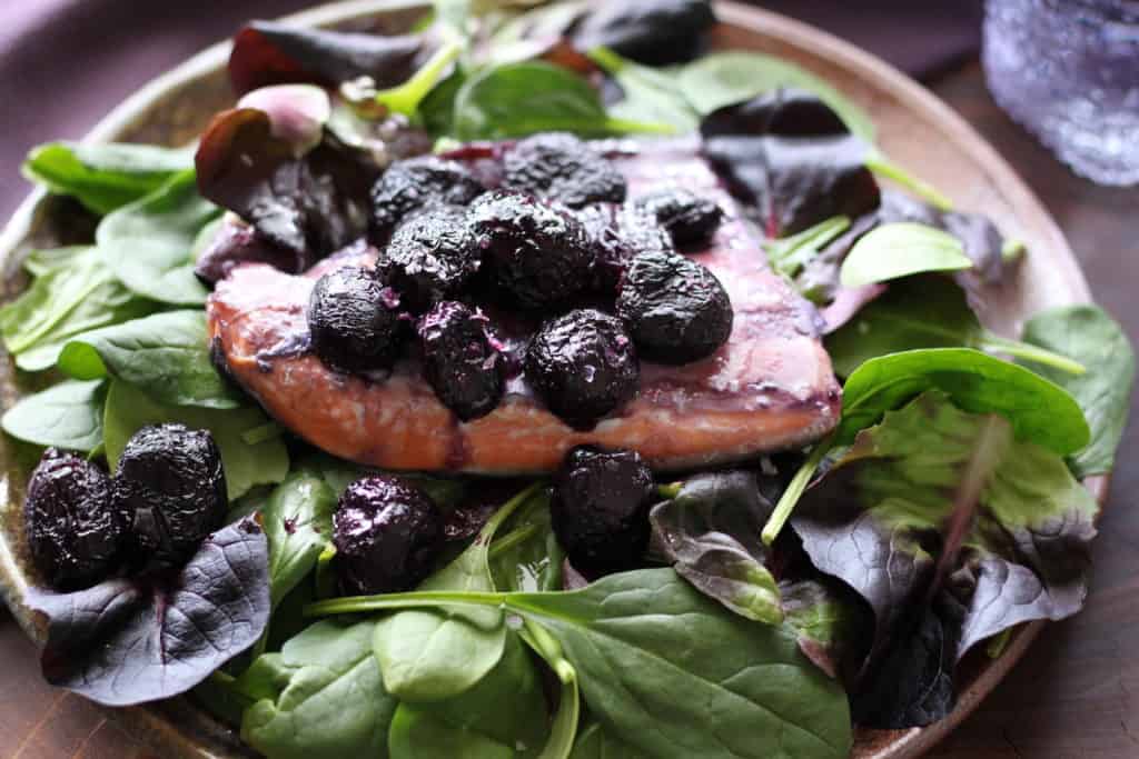 salmon with roasted grapes on plate of fresh spinach
