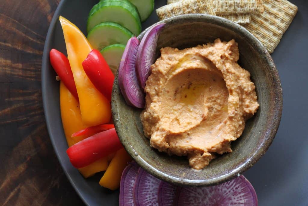 bowl of hummus with crackers, peppers and cucumbers