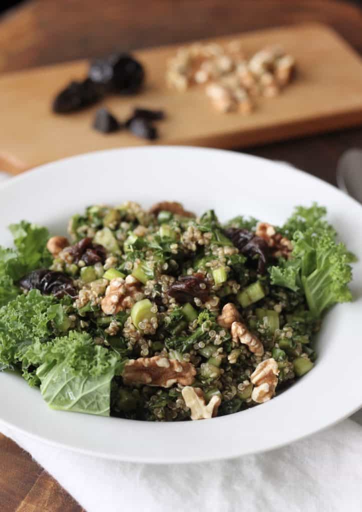 Bowl of kale, quinoa salad with fruit and nuts in background.