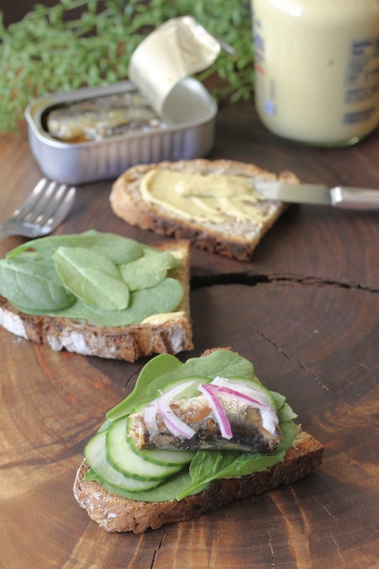 Here's how to make an open-faced sardine sandwich. Mustard, spinach, cucumber, sardines and red onion.