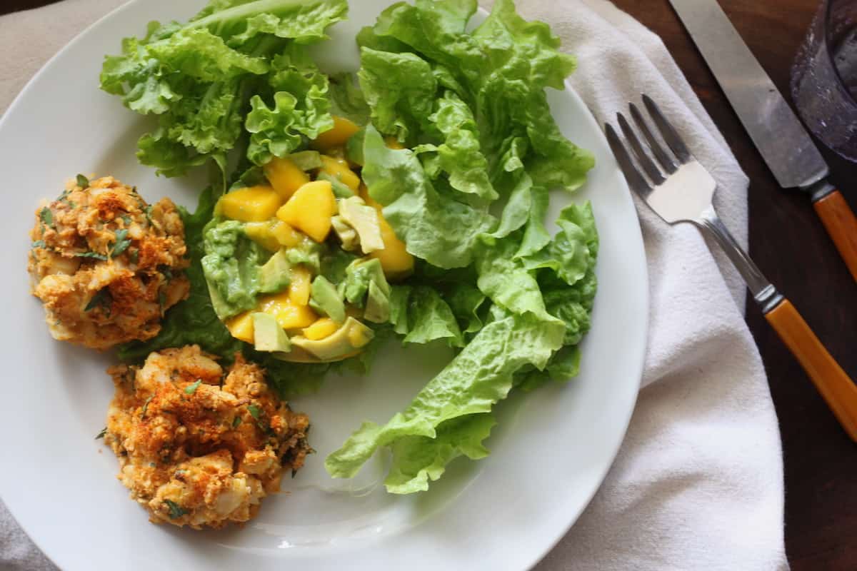 two crab cakes on plate with mango avocado salad