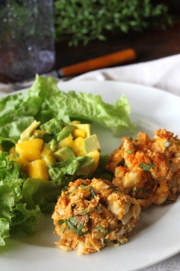 two crab cakes on a plate with mango avocado salad