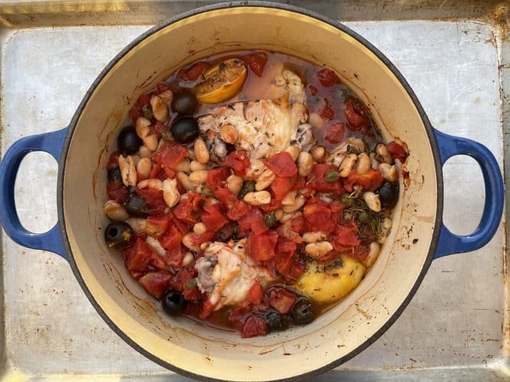 baked chicken in Dutch oven with Bursting with olives, tomatoes, capers, garlic, lemon and beans.