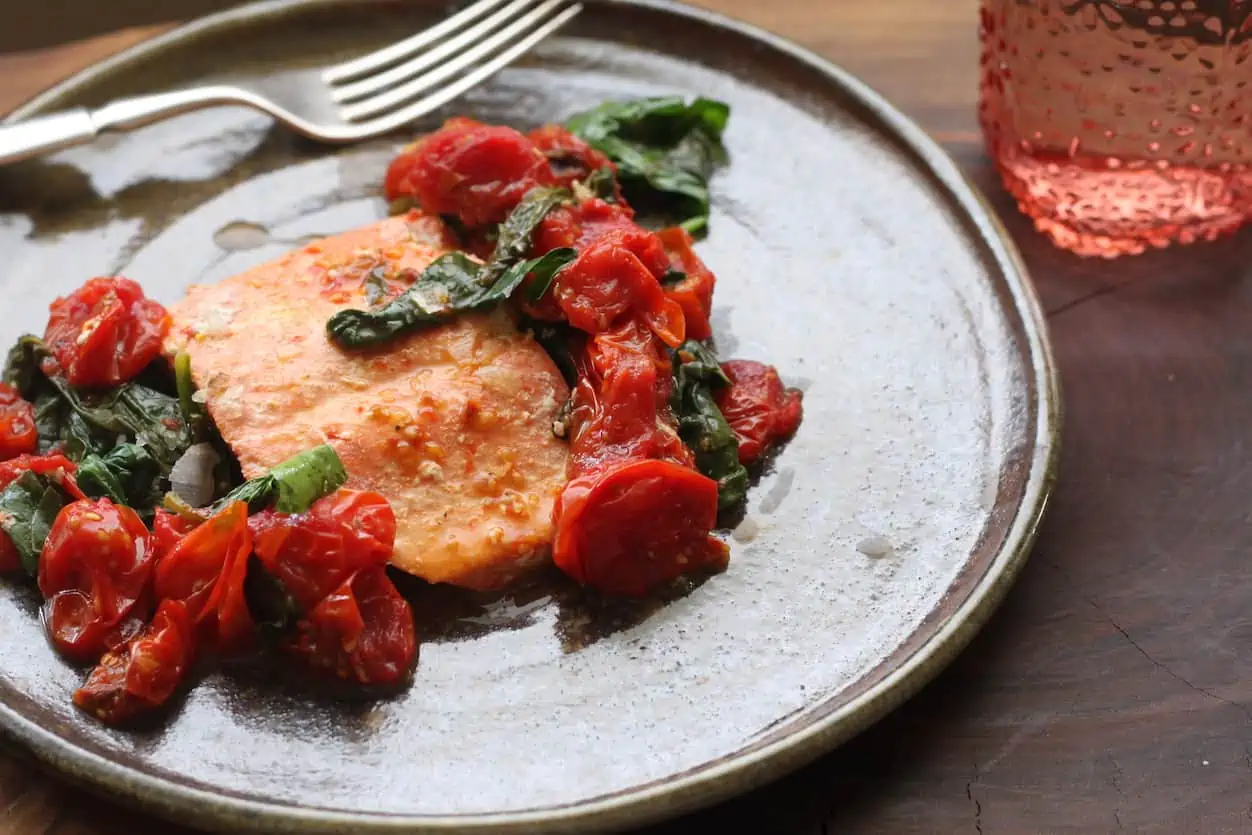 plate with cooked tomatoes and spina cover salmon